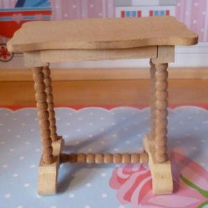 May include: A small wooden table with a rectangular top and beaded legs. The table is made of light brown wood and has a simple design.