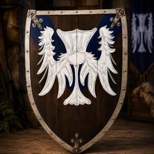 Puede incluir: Un escudo de madera con acabado marrón oscuro y un diseño central de chevrón azul. Un emblema pintado en blanco de un cardo estilizado con alas simétricas está centrado en el escudo. El borde es de color plata metálica con remaches.