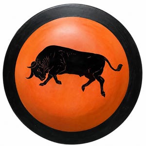Może przedstawiać: Okrągła ceramiczna miska z żywym pomarańczowym wnętrzem i szerokim czarnym brzegiem. W środku miski znajduje się szczegółowa czarna sylwetka byka w pozycji szarżującej, z nisko opuszczoną głową i uniesionym ogonem, co tworzy wyraźny kontrast.