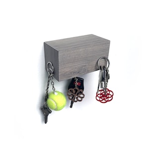 May include: A gray wooden magnetic key holder with a tennis ball, a red geometric design, and a wooden clover charm hanging from it.