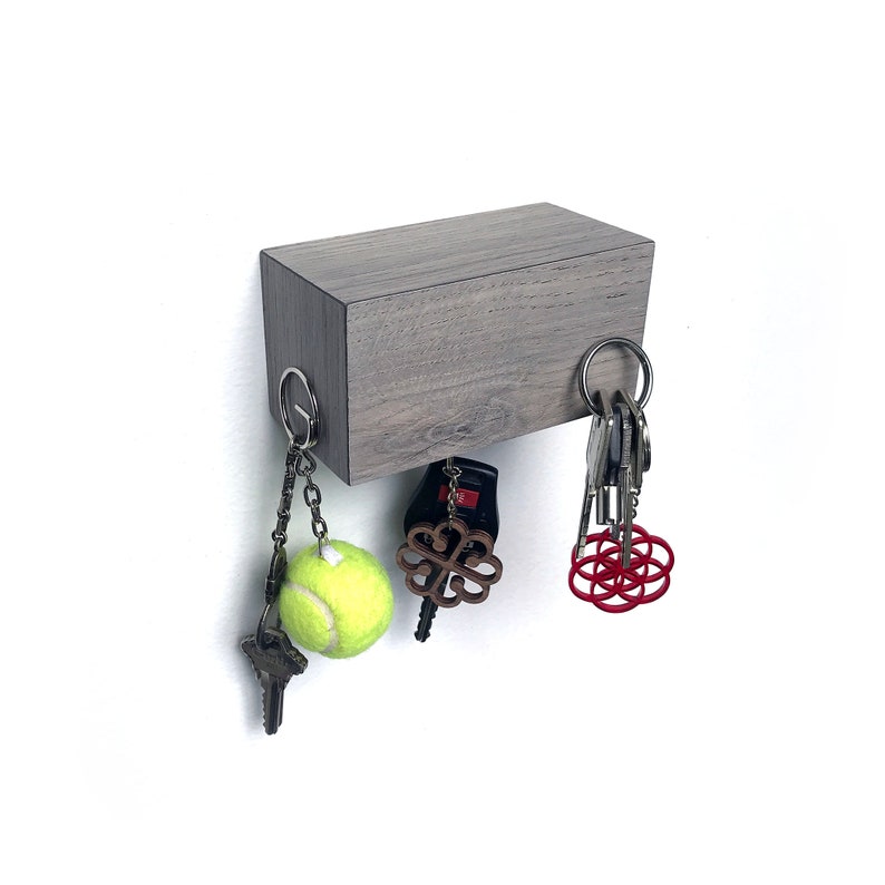May include: A gray wooden magnetic key holder with a tennis ball, a red geometric design, and a wooden clover charm hanging from it.