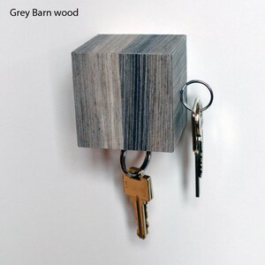 May include: A wooden key holder with a grey and black wood grain finish. The key holder is shaped like a cube and has two sets of keys hanging from it.