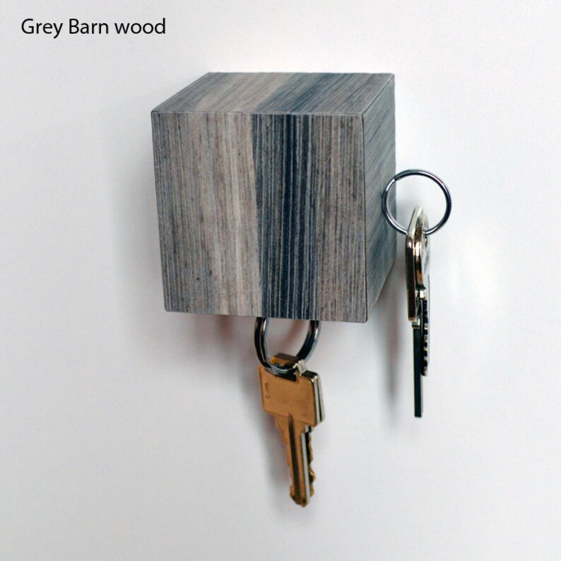 May include: A wooden key holder with a grey and black wood grain finish. The key holder is shaped like a cube and has two sets of keys hanging from it.