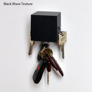 May include: A black wooden key holder with a wave texture. The holder has several keys and key fobs attached to it.
