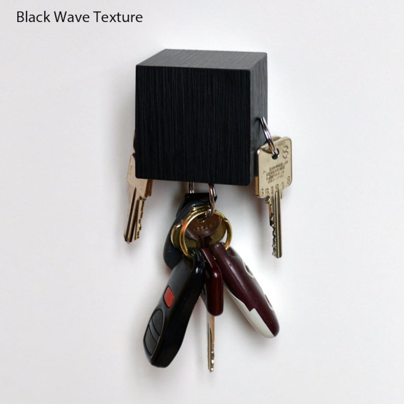 May include: A black wooden key holder with a wave texture. The holder has several keys and key fobs attached to it.