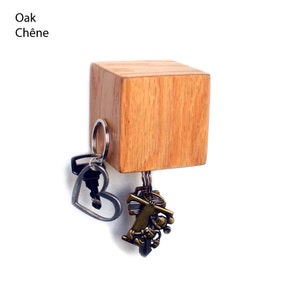 May include: A wooden key holder with a square shape and a natural wood finish. The key holder has a magnetic surface and is holding several keys.