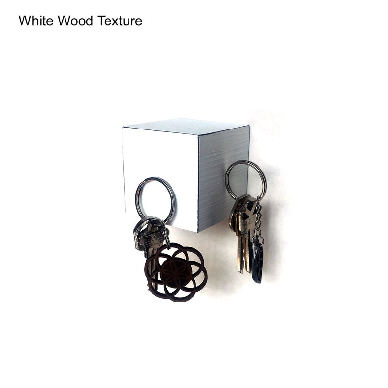 May include: White wooden key holder with a square shape and a textured surface. Two sets of keys are hanging from the holder.