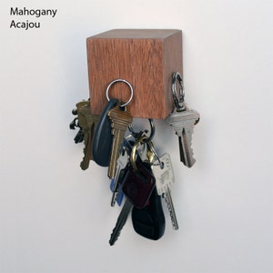 May include: A mahogany wood key holder with a square shape and a magnetic surface.  The key holder is mounted on a white wall and has a variety of keys hanging from it.