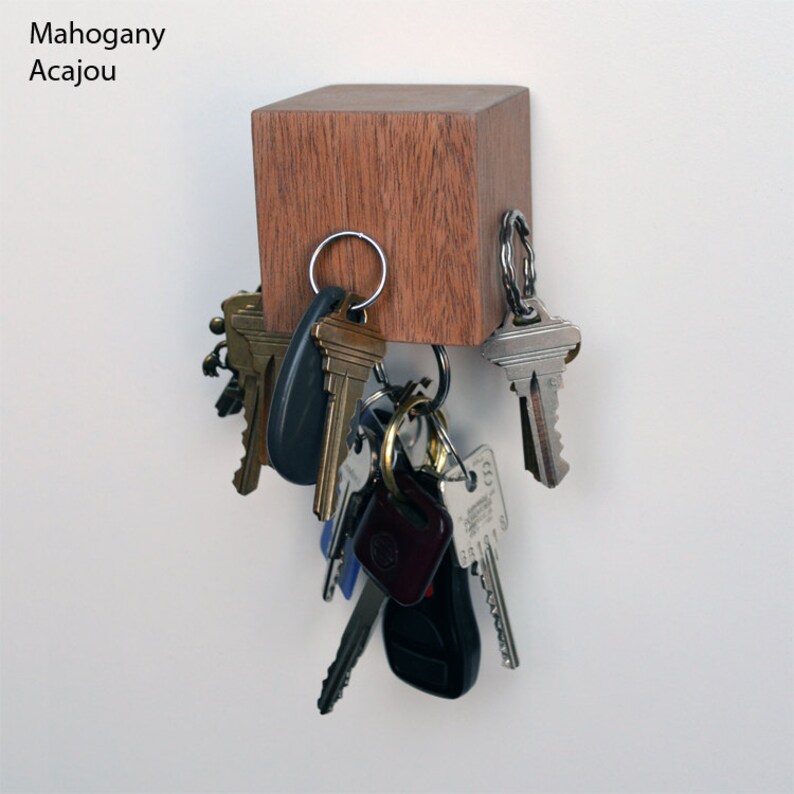 May include: A mahogany wood key holder with a square shape and a magnetic surface.  The key holder is mounted on a white wall and has a variety of keys hanging from it.