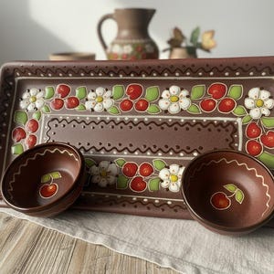 Op de afbeelding: Bruine keramische serveerschaal en twee kommen. De schaal en kommen zijn versierd met een kersen- en bloemmotief in rood, wit en groen. De schaal is rechthoekig met een decoratieve rand.