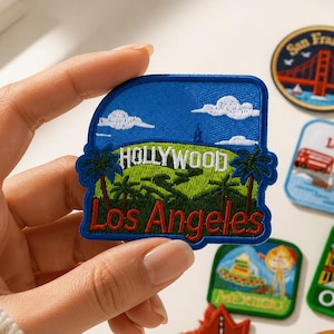 Può includere: Una collezione di toppe ricamate souvenir raffiguranti vari monumenti e città globali. Le toppe includono disegni per Hollywood Los Angeles, San Francisco, Londra, Messico, Osaka, Canada e Tokyo, ognuna con colori e testo distinti.