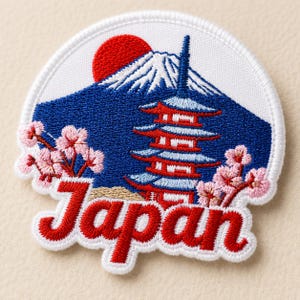 May include: A circular embroidered patch featuring a blue mountain with a white snow-capped peak, a red sun, a multi-tiered red and blue pagoda, and pink cherry blossom branches. The word Japan is stitched in red cursive script at the bottom.