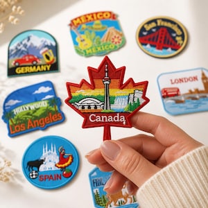 Pode incluir: Uma coleção de emblemas bordados de lembrança com vários marcos e locais globais. O emblema central tem a forma de uma folha de bordo vermelha com o texto Canada, retratando a CN Tower, um estádio e uma cascata sob um céu de arco-íris.