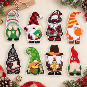 Pode incluir: Oito emblemas bordados de gnomos com vários temas sazonais. Os gnomos usam chapéus e roupas coloridas, com padrões xadrez, listrados ou cores sólidas. Eles seguram itens como uma pequena árvore, uma abóbora, um pote de ouro e um livro.