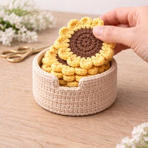 May include: A set of handmade crochet sunflower coasters in a beige basket. The coasters have yellow petals and a brown center. The basket is also beige and has a small cutout on one side.