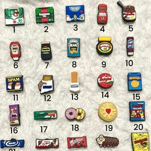 May include: A collection of thirty small, colourful rubber shoe charms arranged in a grid, each featuring miniature designs of popular food and beverage brands, including cereal boxes, condiment bottles, chocolate bars, and various snack items.
