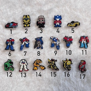 Puede incluir: Colección de diecisiete amuletos coloridos con temática de robots. Los amuletos presentan varios diseños de robots en rojo, azul, amarillo y verde. Estos amuletos son adecuados para zapatos, pulseras u otros accesorios.