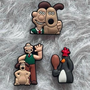 Peut inclure: Trois breloques en caoutchouc pour chaussures représentant les personnages de Wallace et Gromit. Une breloque montre Wallace et Gromit côte à côte, une autre Wallace debout avec Gromit, et la troisième un pingouin tenant une cuisse de poulet.