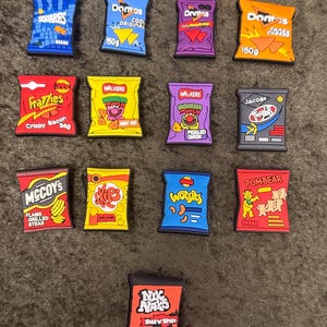 May include: A selection of chip bag charms, featuring brands such as Doritos, Walkers, and Nik Naks. The charms are in various colours, including blue, red, yellow, and orange, with text and graphics. The bags are in various sizes.