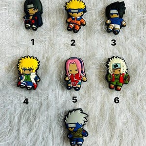 Peut inclure: Un ensemble de sept breloques en caoutchouc pour chaussures représentant divers personnages d'anime. Chaque figurine est numérotée de un à sept, arborant des tenues et des coiffures distinctes dans des tons de noir, jaune, bleu, rouge, rose, vert et blanc.