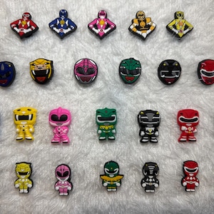 Op de afbeelding: Een verzameling kleurrijke schoenbedels met Power Ranger-thema. De bedels tonen verschillende personages in verschillende kleuren, waaronder rood, blauw, geel, roze, groen, zwart en oranje. Sommige bedels zijn gevormd als de helmen van de Rangers.
