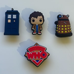 Könnte beinhalten: Vier Doctor Who-Charms. Enthält eine blaue TARDIS, eine Figur des Doktors, einen Dalek und ein rot-weiß-blaues Doctor Who-Logo. Diese Charms sind wahrscheinlich aus Gummi oder Kunststoff und sind dekorativ.