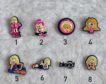 May include: A collection of eight colorful shoe charms featuring a cartoon character with blonde hair. The charms depict the character in various poses and outfits, including a pink outfit, a cowboy hat, and the word "blond".