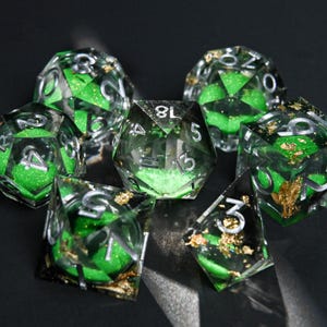 May include: A set of polyhedral dice. The dice are clear with green glitter and silver numbering. Some dice have gold leaf inclusions. These dice are designed for tabletop role-playing games.