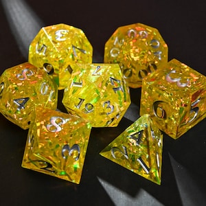 May include: A set of seven yellow resin dice with silver numbering. The dice are various shapes, including a d4, d6, d8, d10, d12, d20, and a percentile die. The dice are filled with iridescent glitter.