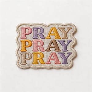 May include: Embroidered patch with the word "PRAY" repeated three times in different colors: pink, purple, yellow, and brown. The patch has a beige border with a scalloped edge. The text is in a serif font.