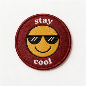 May include: Embroidered patch featuring a yellow smiley face wearing black sunglasses, set against a maroon circular background. The words "stay cool" are embroidered in white, arching above and below the emoji.
