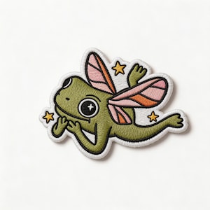 May include: Embroidered patch featuring a whimsical green frog with pink and orange fairy wings, and three yellow star accents. The frog is smiling and has a white outline.