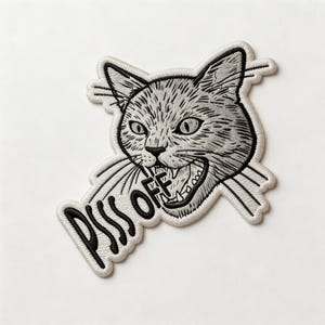 May include: Embroidered patch featuring a gray cat's head with an open mouth and the words "PISS OFF" in black. The patch has a white border and is designed to be ironed or sewn onto fabric.