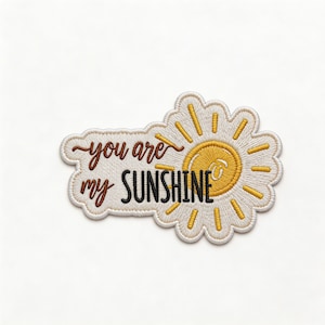May include: Embroidered patch with the phrase "you are my sunshine" in brown and black lettering. The patch features a yellow sun design with radiating rays, all outlined in a cream color.