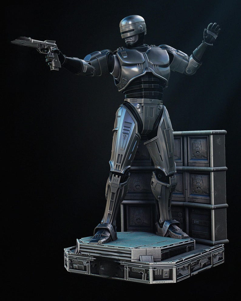Puede incluir: Una figura de acci&oacute;n de RoboCop de color gris met&aacute;lico, posando con una pistola en una mano y la otra mano levantada. La figura se encuentra sobre una plataforma con una superficie azul, con una pila de contenedores de almacenamiento grises detr&aacute;s.
