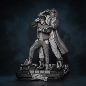Può includere: Statua in scala di grigi dei personaggi del film "Ritorno al futuro II". La statua presenta due figure in piedi su una piattaforma con il titolo del film. Una figura indossa una giacca e pantaloni, l'altra un cappotto lungo e occhiali.
