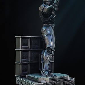 Puede incluir: Estatua detallada de Robocop, una figura plateada y negra en una pose din&aacute;mica, sosteniendo un arma. La estatua tiene intrincados detalles de armadura y se alza sobre una plataforma con un dise&ntilde;o futurista, sobre un fondo oscuro.