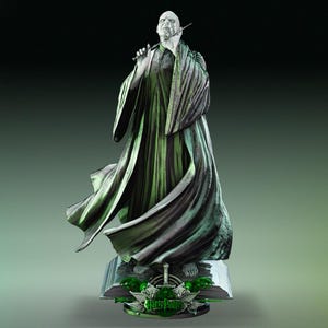 Op de afbeelding: Een standbeeld van een kale figuur in lange, vloeiende gewaden, met een toverstaf. Het standbeeld is overwegend groen en grijs, met ingewikkelde details. De basis toont de woorden "Harry Potter" en andere decoratieve elementen.