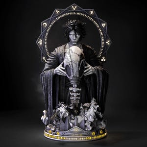 Può includere: Statua dettagliata di una figura in abiti scuri che tiene in mano un grande oggetto ornato. La statua ha una combinazione di colori scuri con dettagli intricati, tra cui una struttura a forma di alone dietro la testa della figura. La base presenta elementi scolpiti e testo aggiuntivi.