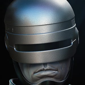 Puede incluir: Primer plano de un casco plateado met&aacute;lico con visera y parte superior redondeada. El casco tiene un dise&ntilde;o futurista, con un fondo oscuro. La cara de una persona es visible debajo de la visera.