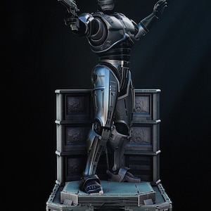 May include: A metallic silver and blue RoboCop statue, holding a gun in its right hand and its left hand raised. The statue is standing on a platform with a detailed base and a dark background.