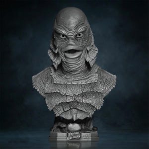 Peut inclure: Buste gris du monstre de l'Étrange Créature du Lac Noir. La sculpture présente des textures détaillées et les traits de visage emblématiques de la créature. La base comprend le texte "Creature Black Lagoon".