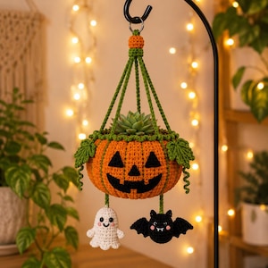 May include: A crocheted orange pumpkin planter with a jack-o'-lantern face, green leaves, and hanging charms of a white ghost and a black bat. The pumpkin holds a green succulent plant and is suspended by green crocheted cords from a metal hook.