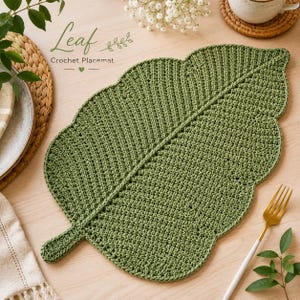May include: A green crochet leaf-shaped placemat. The placemat has a detailed texture and a central vein design. The words "Leaf" and "Crochet Placemat" are written on the top left of the image.