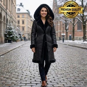 May include: A long black coat with a hood and fur trim. The coat is buttoned up and worn by a person walking on a cobblestone street. The coat has fur trim on the hood, cuffs, and along the front opening. The background shows a snowy street scene.