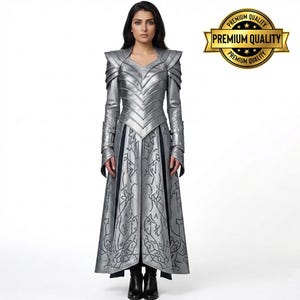 May include: A silver-colored, long-sleeved dress with intricate detailing and a V-neckline. The dress features a structured bodice and a flowing skirt with a patterned design. The image includes a "Premium Quality" gold seal.