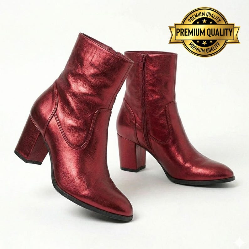 May include: A pair of shiny, red ankle boots with block heels. The boots have a metallic finish and a side zipper. The boots are displayed on a white background. A gold "Premium Quality" seal is in the background.