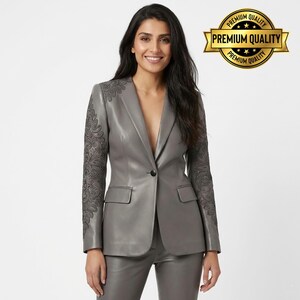 Pode incluir: Um blazer de couro cinza com bordados pretos intrincados nas mangas. O blazer tem um fecho de um bot&atilde;o e dois bolsos frontais. Cal&ccedil;as cinza combinando tamb&eacute;m s&atilde;o vis&iacute;veis. O texto "PREMIUM QUALITY" &eacute; exibido em um emblema dourado.