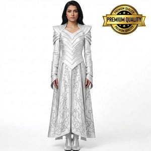 May include: A white, long-sleeved gown with intricate silver detailing. The dress features a V-neckline, structured shoulders, and a flowing skirt with a patterned design. The image includes a gold "Premium Quality" seal.