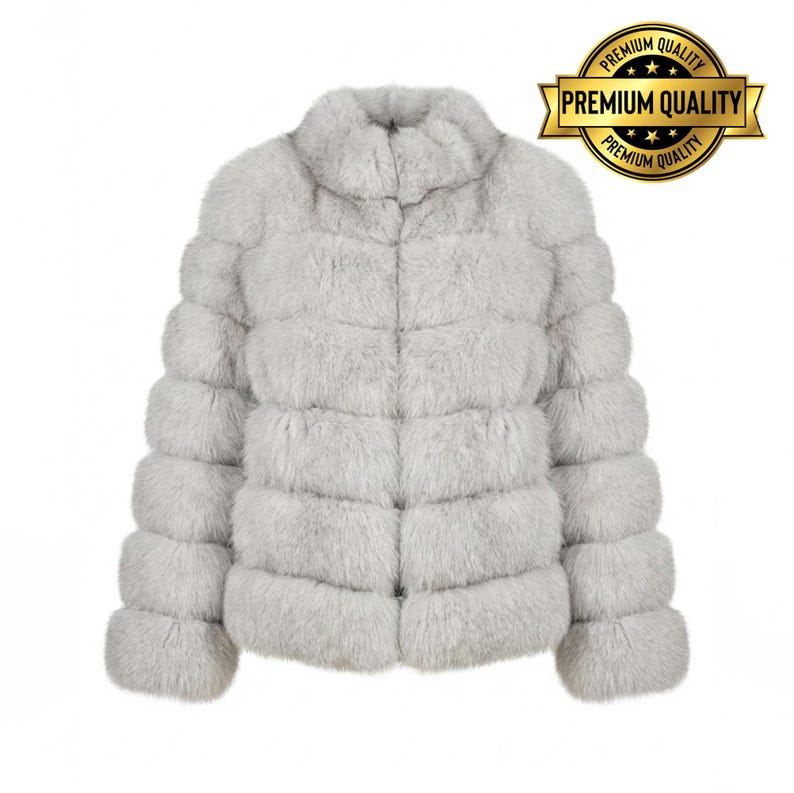 May include: A light gray faux fur jacket with a high collar and horizontal panel design. The jacket has long sleeves and a soft, textured appearance. A gold seal with the words "Premium Quality" is in the upper right corner.